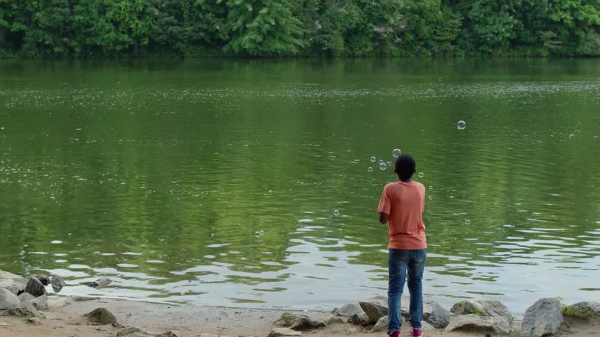 A boy blows bubbles on a lakeshore