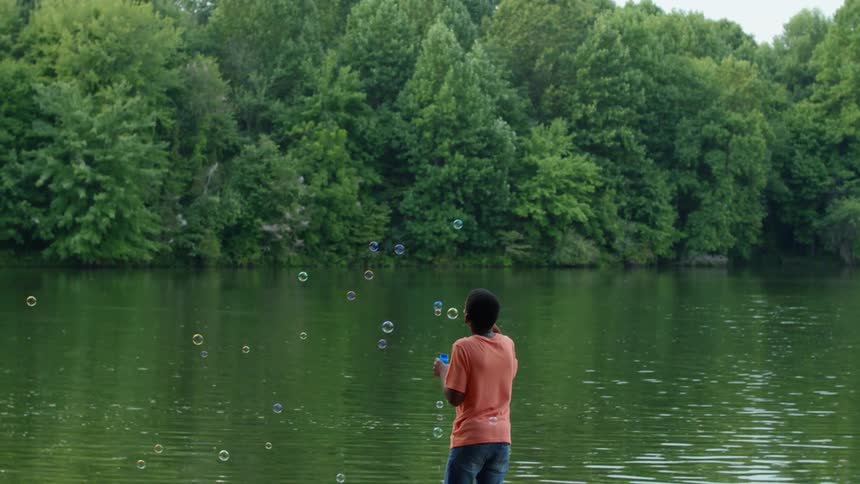 A boy blowing soap bubbles next to a river