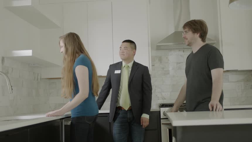 Real estate agent shows man and woman the kitchen in day time