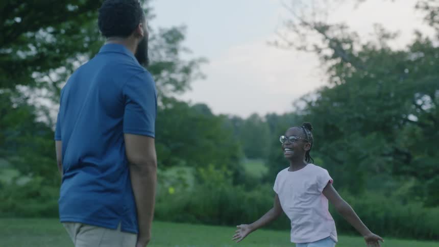 A father and daughter walk on a grassy lawn