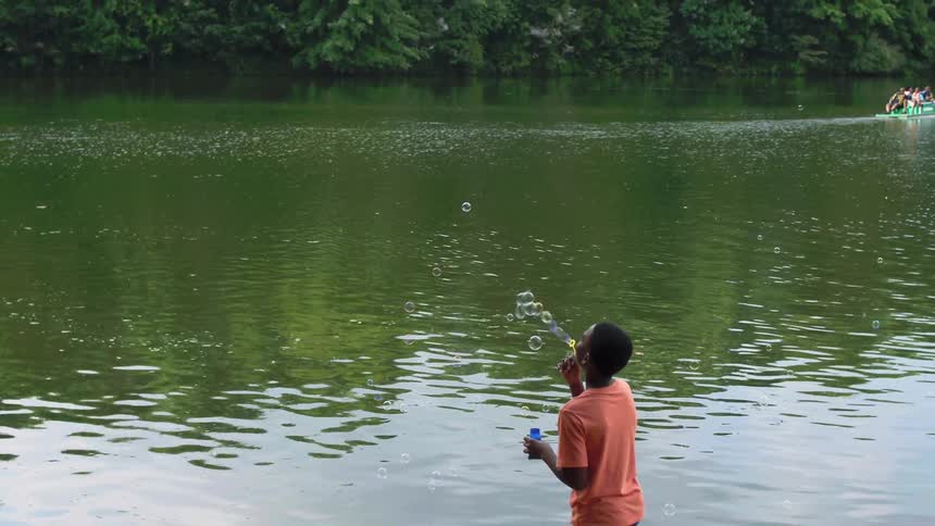A boy blows bubbles next to a rippling lake