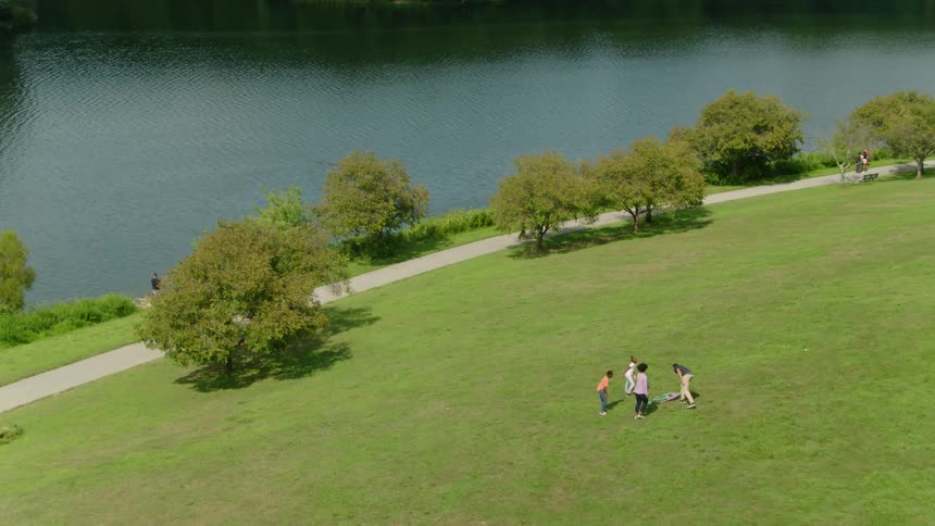 A family of four flying a kite in a park near a river and trees