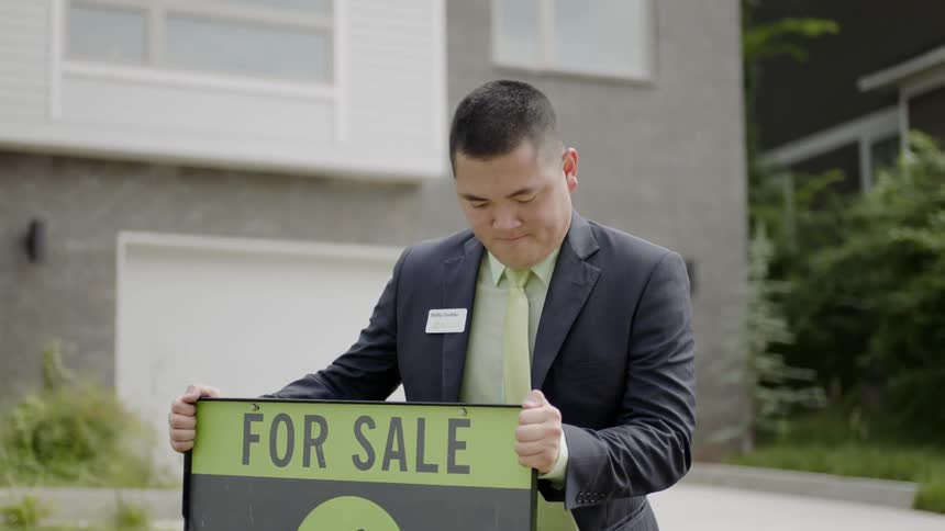 A man is putting a fore sale sign outside a house