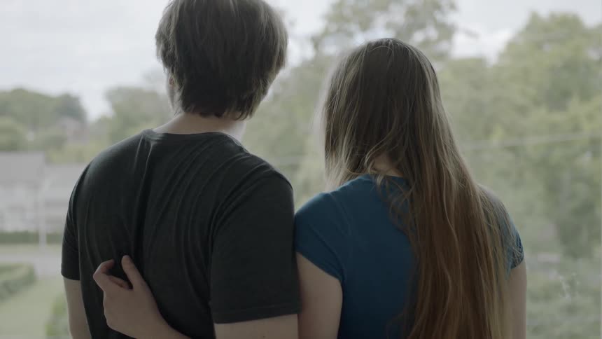 A young couple hug while looking out a window