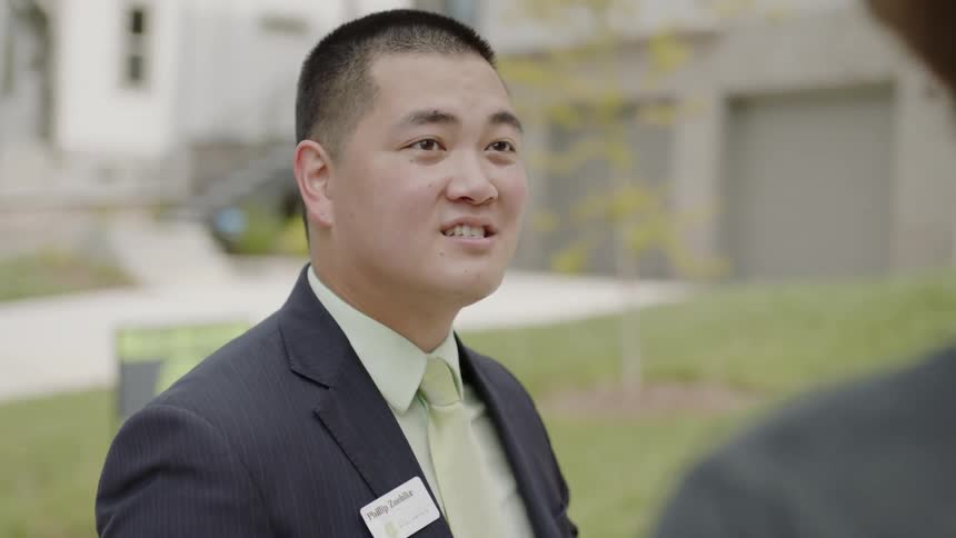 A man in wearing a name badge in a lounge suit talks to a casually dressed man and points towards real estate