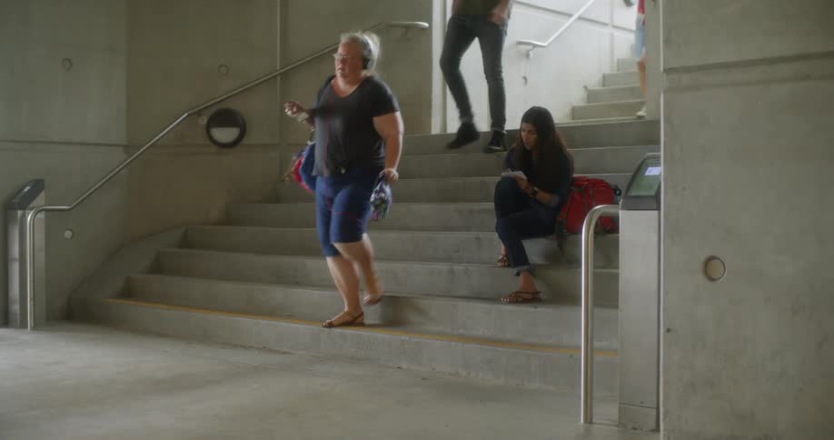 Girl studies on stairs while people pass by her underground