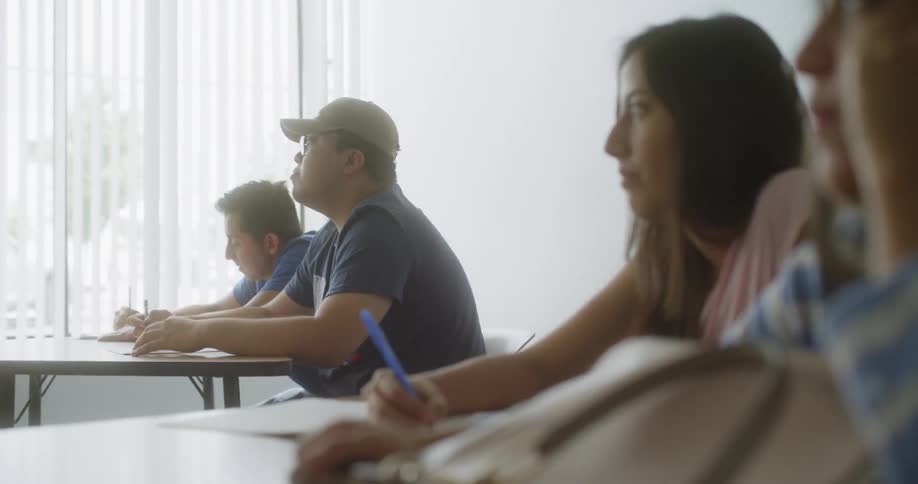 Students sit at tables and take notes on a sunny day