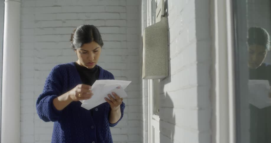 A young woman takes a letter out of the mailbox, opens it, and reads it