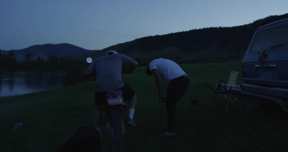 Two men use a dirt bike next to a lake at dusk