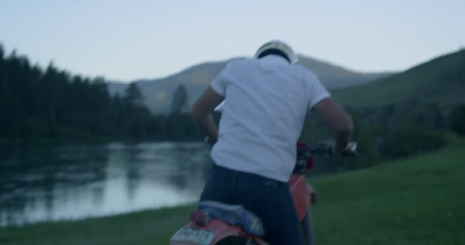 A man near a pond gets on his motorcycle