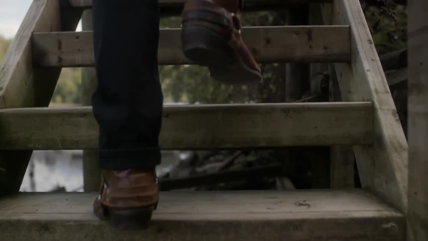 A man in cowboy boots walking up wooden stairs