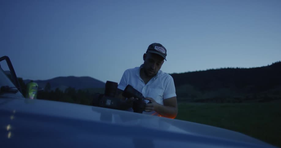 A man is outside by his car putting together a camera