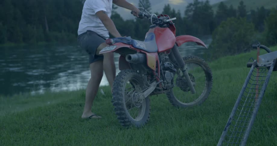 A man stands up his dirt bike by a river