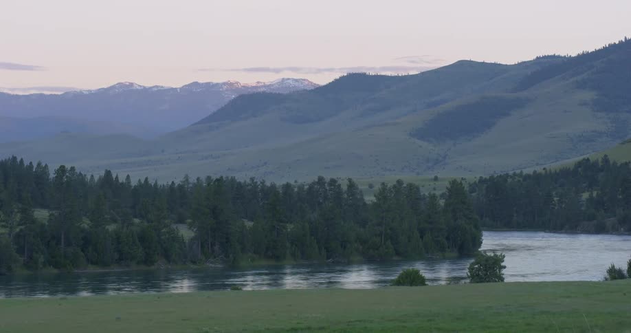 A river flows past trees at the base of hills at sunset
