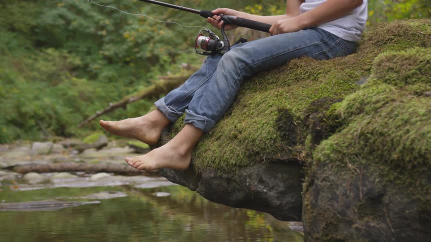 A boy fishes from a mossy rock