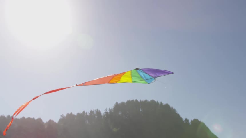 A rainbow colored kite flies through the sky
