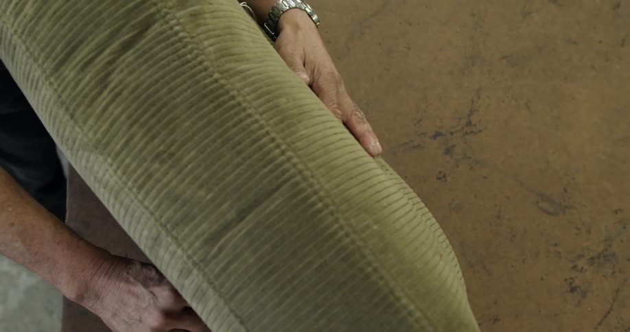 Man holding a large cushion puts a rod through it and grabs string