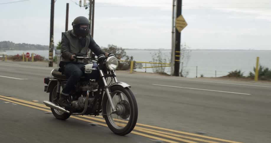 Person riding a motorcycle down a road near the shore