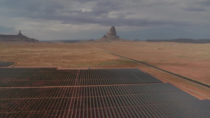 Cars driving on the road in the desert next to a solar panel field