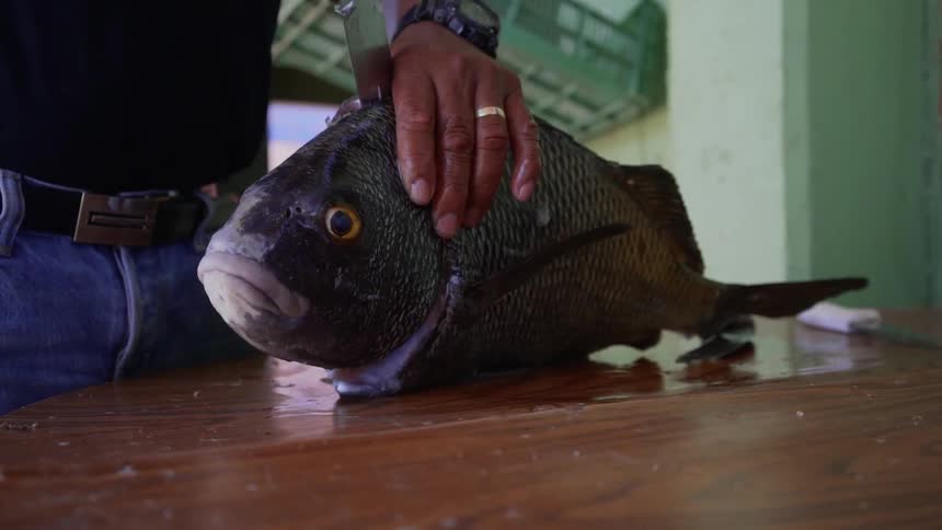 A man is cutting a fish in the kitchen