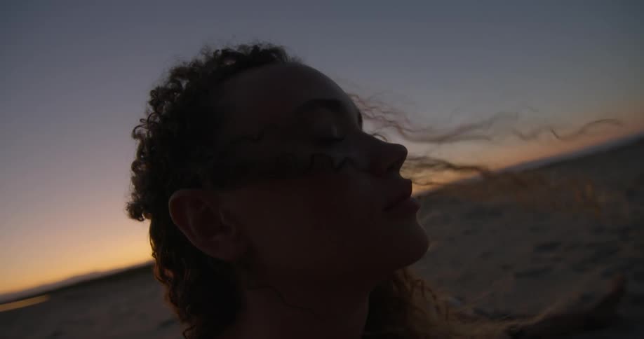 Wind blows through a woman's curly hair in a desert at sunset