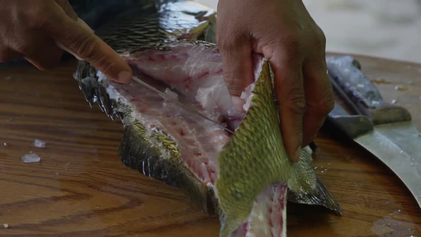 Man cleans fish with knife on cutting board