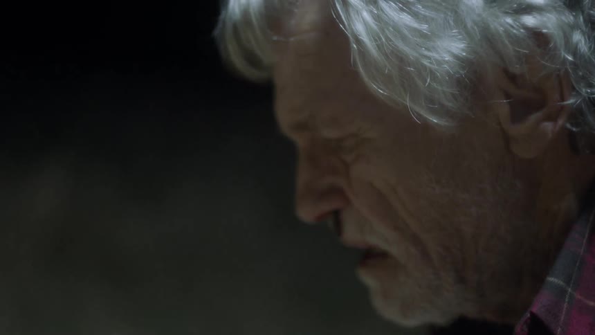 Injured elderly man looking at bloody hands with smoke nearby