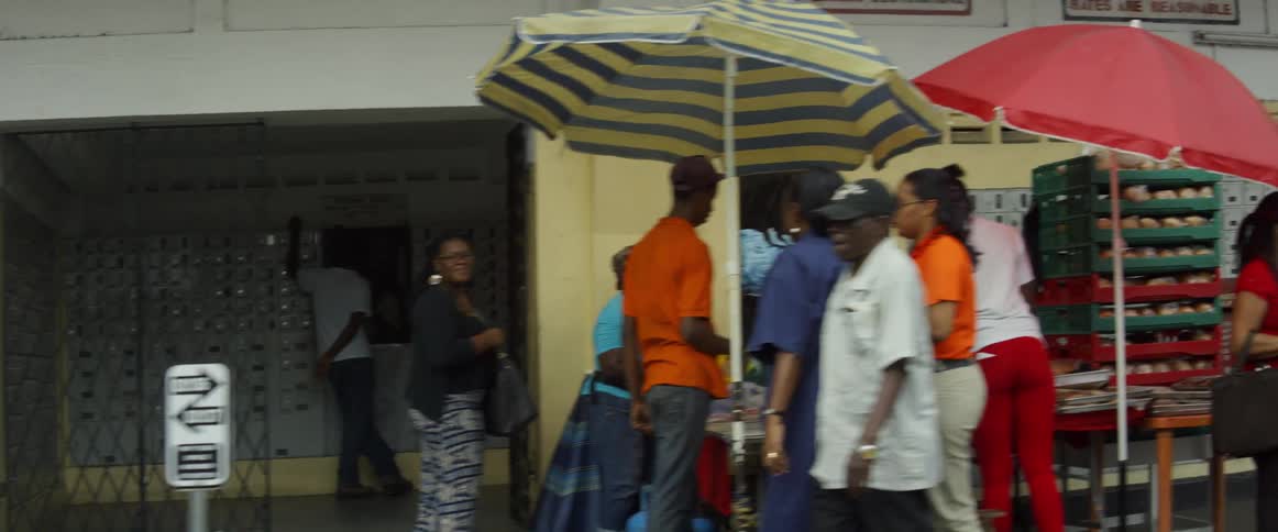 People walk on pavement while cars drive in city center on a cloudy day