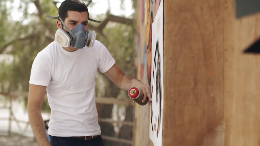 A man uses a stencil and spray paint on an exterior wall