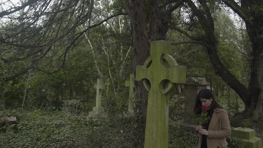 A woman holds red roses next to a grave in a cemetery