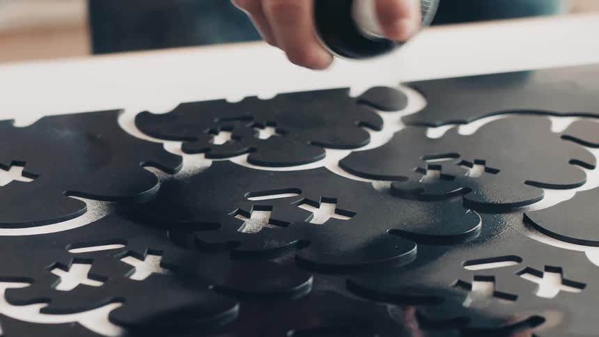 A person spray painting black paint on a black stencil and canvas