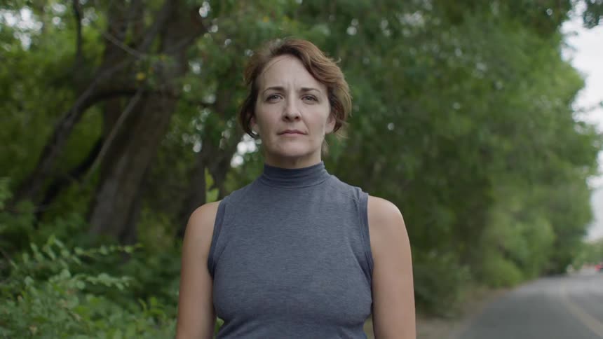 A woman is standing outside in a wooded area
