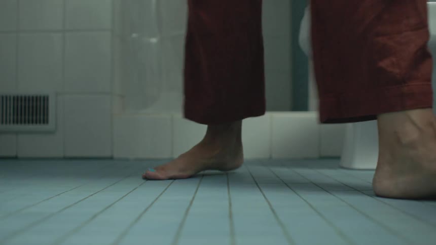 A person stands up from the toilet and walks to the left