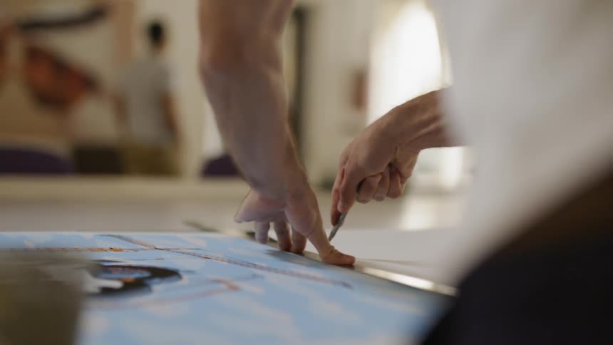 A man uses an exacto knife to cut a white sheet of material