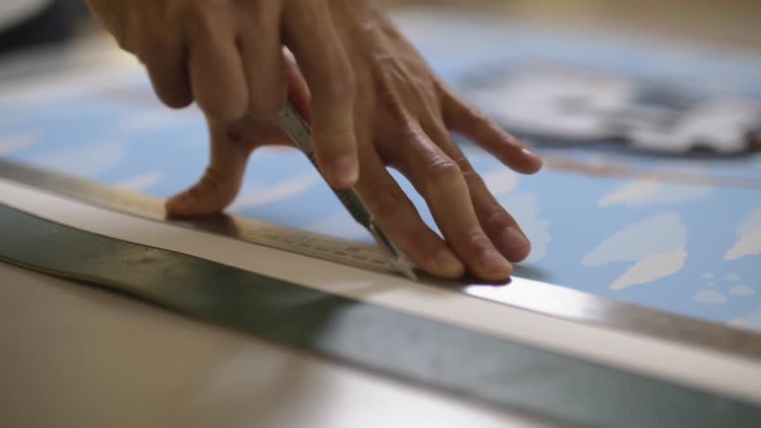 A person cuts a piece of paper with a blade and ruler