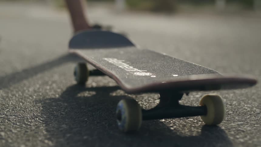 A person wearing sneakers walks up to a skateboard on a road on a sunny day