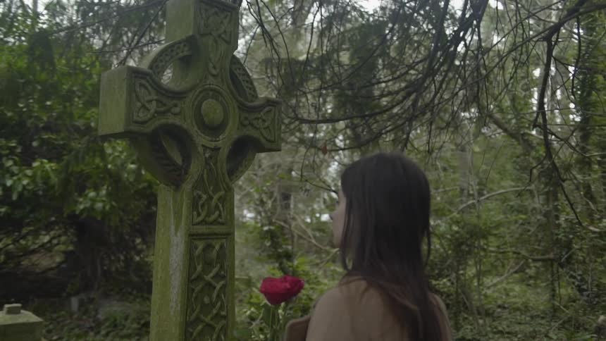 Woman walking up to a statue in a cemetery while carrying roses