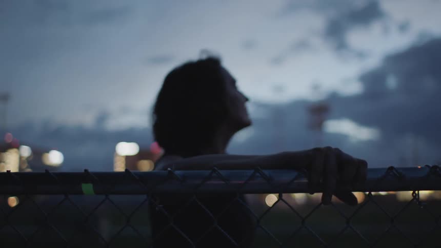 Woman leans on wire fence then getting up at dusk