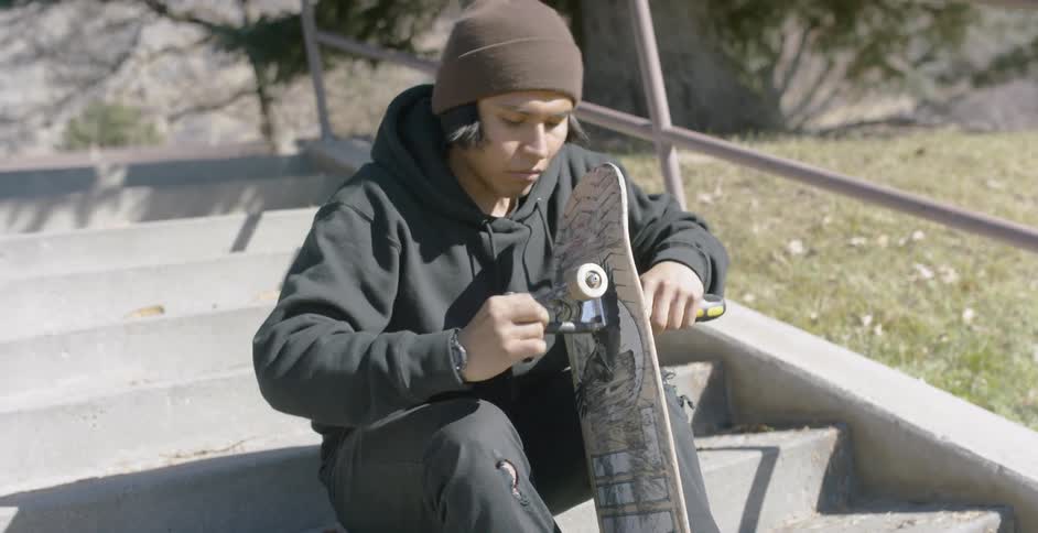 A man is fixing a skateboard while sitting down