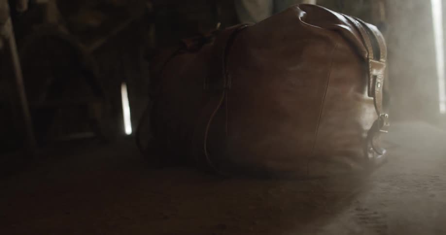 Man drops a carry-on leather bag and dust stirs up
