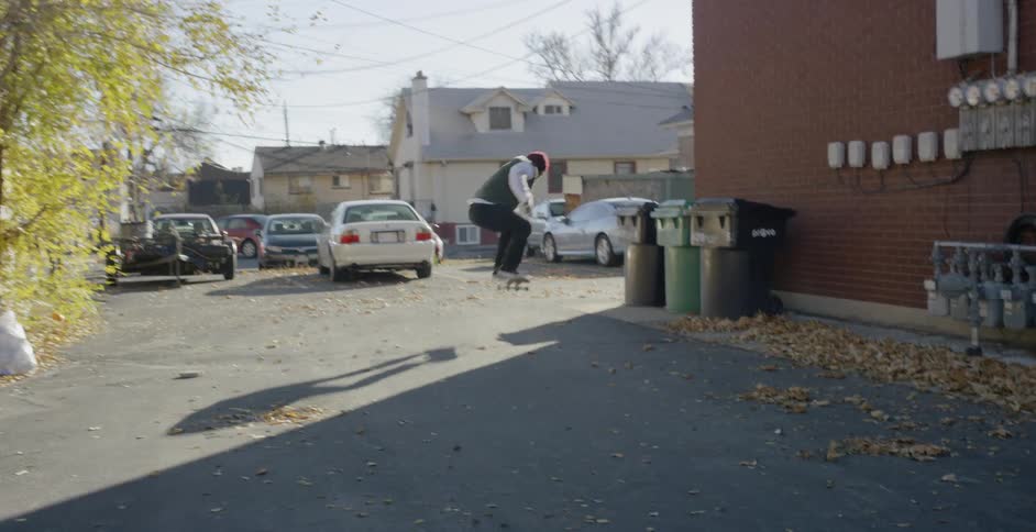A boy riding and jumping on his skateboard in an alley