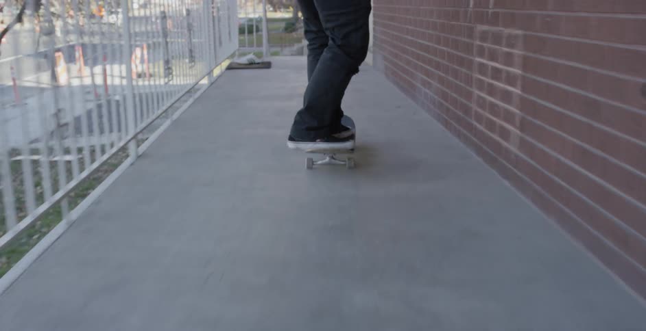 A person skateboarding down an exterior hallway and stops at the top of stairs