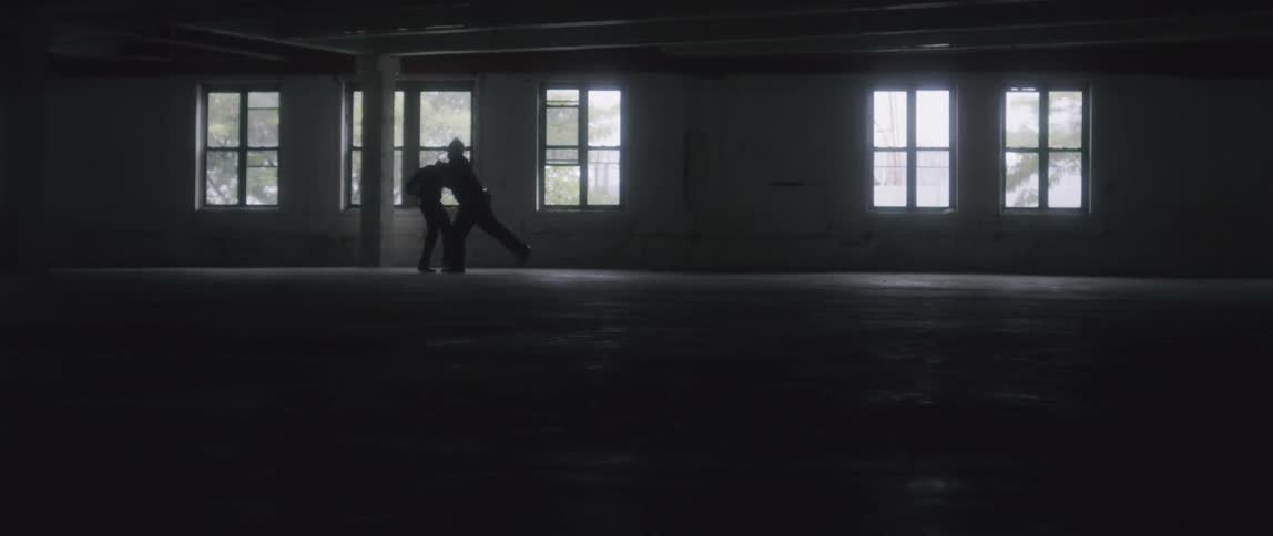 Two people in an empty room physically fighting each other