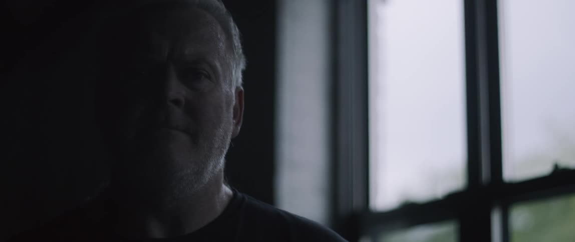 A man stands by the window in a dark building