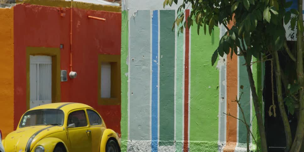 A yellow car in front of a colorful wall