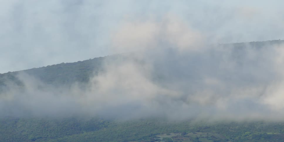 Clouds float above a green misty mountain