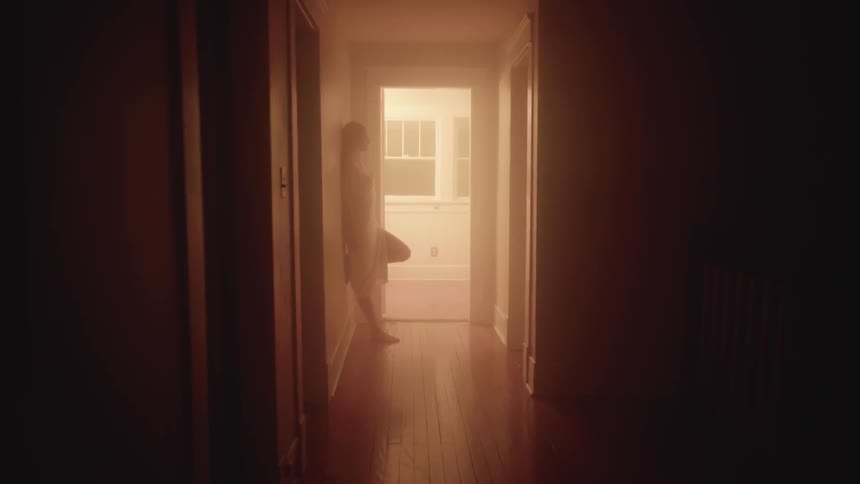 A woman leans against a wall in a hallway at night