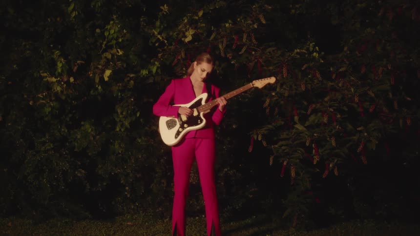 A woman in a pink suit plays guitar in front of trees at night