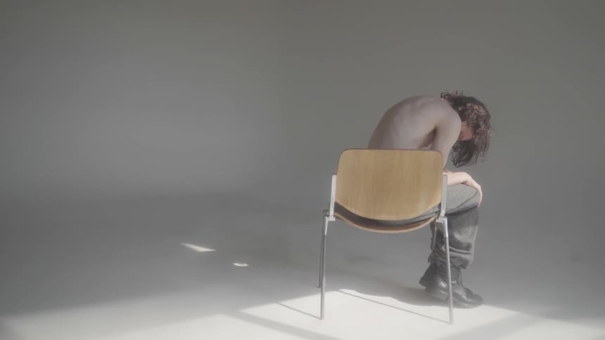 Scared shirtless person sitting on chair in middle of room