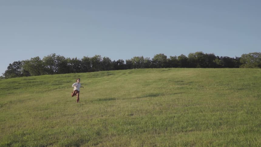 A guy runs down grassy hill